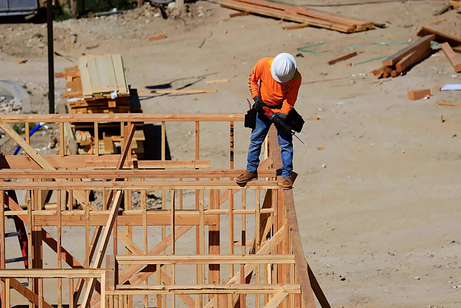 Construction worker in a hard hat using a drill on wooden house framing at a residential site