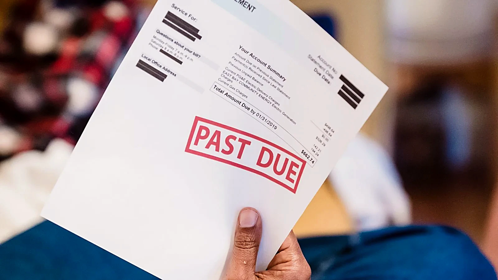 Hand holding a bill stamped PAST DUE in red