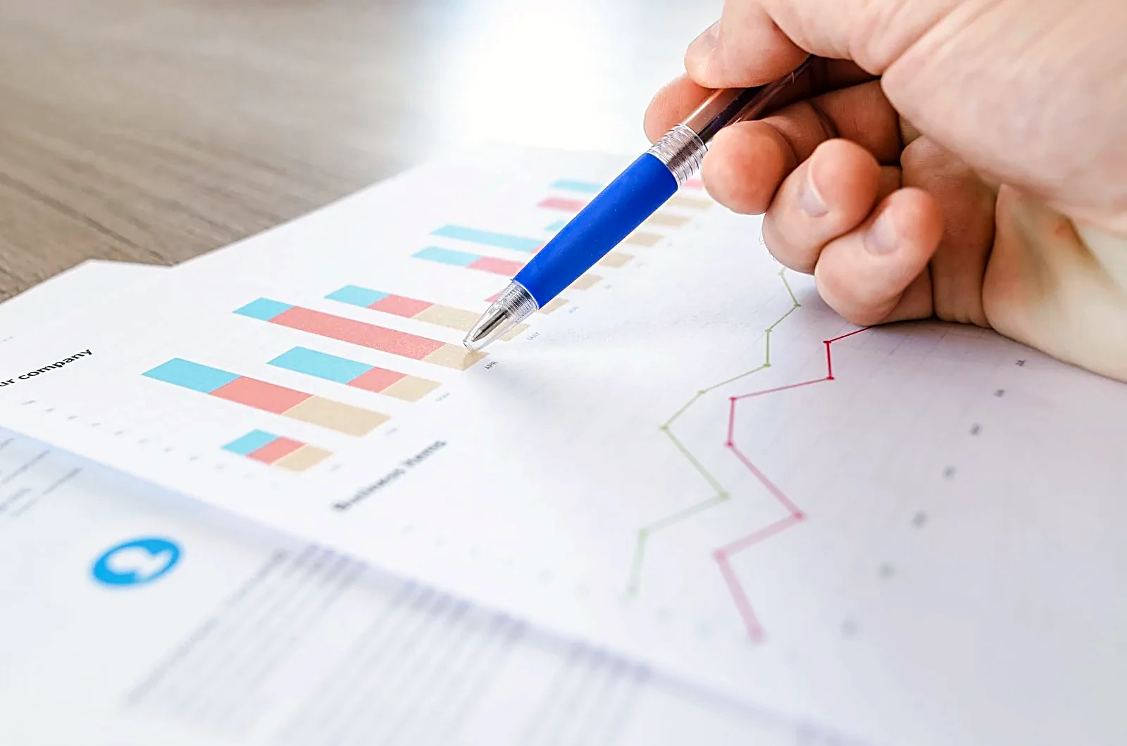 Hand with a pen pointing at bar and line charts on paper