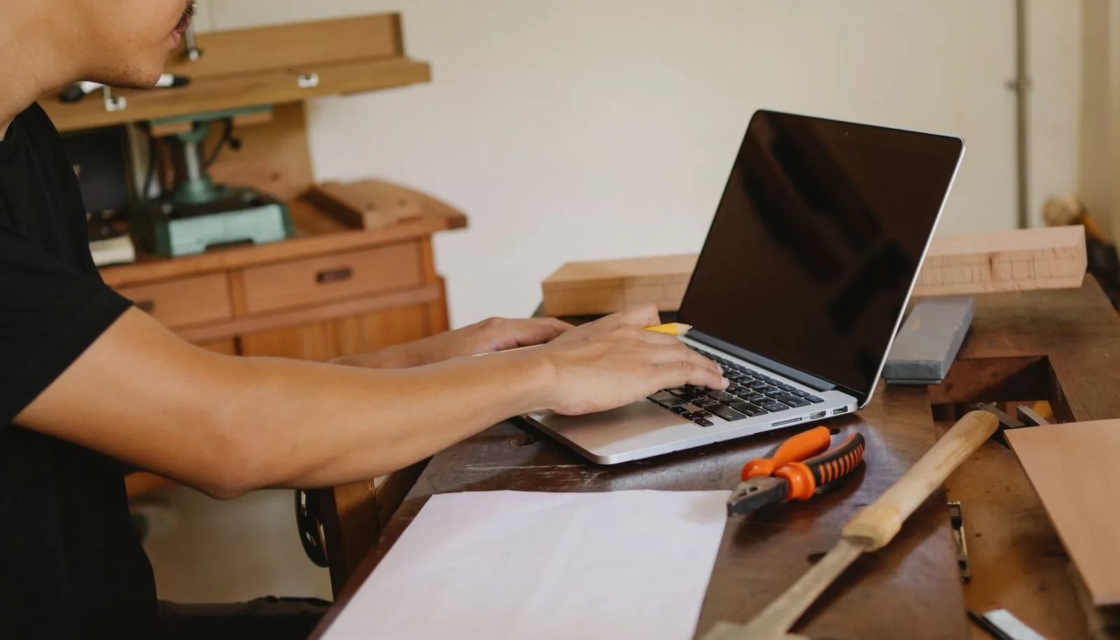 Contractor working on a laptop at a workbench with hand tools