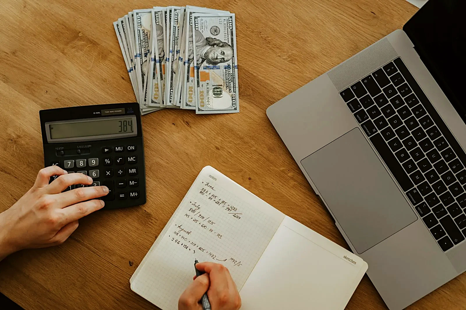 Calculator, cash, notebook, and laptop on a wooden desk