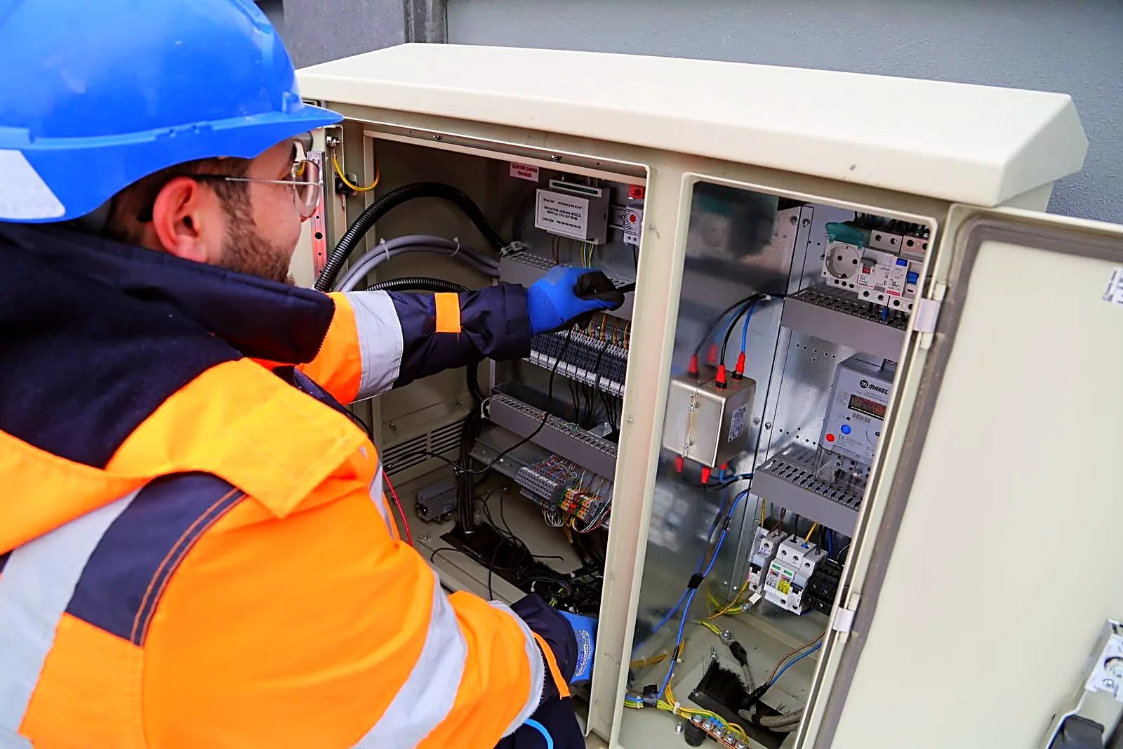 Electrician in a hard hat and hi-vis vest working on an open electrical cabinet