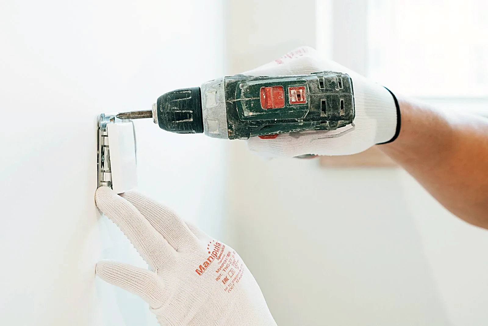 Gloved hands installing an electrical outlet with a drill