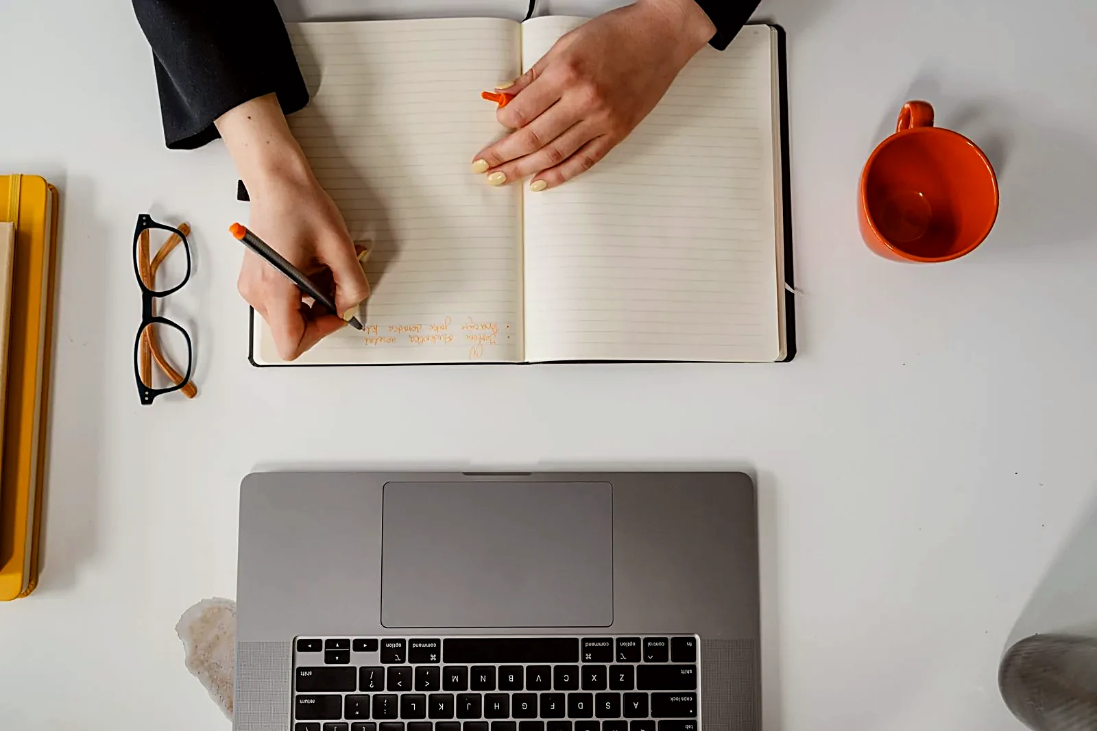 Notebook, laptop, and coffee on a white desk, overhead view