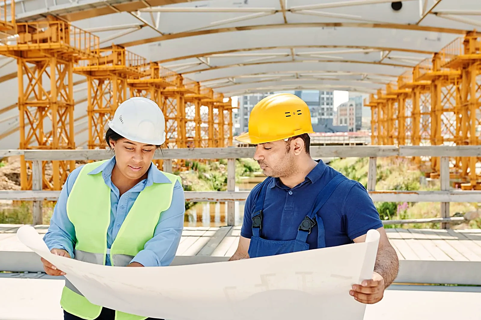 Two construction professionals in safety gear reviewing a blueprint on site